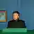 Mann im schwarzen Anzug sitzt hinter grün drapiertem Tisch vor blauer Wand. Links neben ihm ein Porträt an der Wand (Quelle: AP)