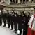 Sieben Männer und Frauen in dunklen Anzügen heben die rechte Hand zum Eid. Rechts und links der Gruppe je ein Mann in rot-weißer Tracht (Quelle: AP)