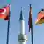 A minaret stands between a Turkish flag and a German flag