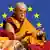 Dalaj Lama sjedi ispred pozadine obojene plavom bojom sa žutim zvjezdicama - simbolom Europske unije
