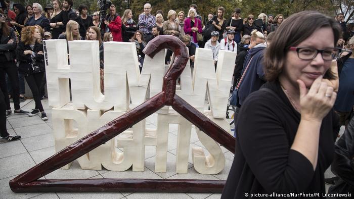 Участницы акции в Варшаве стоят за большой вешалкой для одежды и сложенной из белых букв надписи Право человека