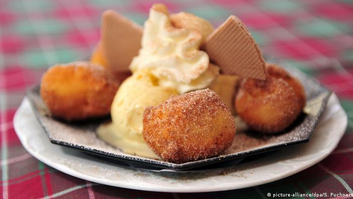 Panecillos redondos fritos y espolvoreados con azúcar, junto a una bola de helado de vainilla.