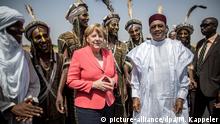 10.10.2016+++ Bundeskanzlerin Angela Merkel (CDU) wird am 10.10.2016 in Niamey im Niger von Präsident Mahamadou Issoufou (r) sowie Männern vom Stamm der Wodaabe begrüßt. Kanzlerin Merkel befindet sich auf einen dreitägigen Reise durch Afrika mit Stationen in Mali, Niger und Äthiopien. +++ (C) picture-alliance/dpa/M. Kappeler
