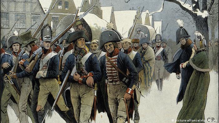 александровка в германии история. 36339680 303. александровка в германии история фото. александровка в германии история-36339680 303. картинка александровка в германии история. картинка 36339680 303. В северной части Потсдама есть место столь русское, какой даже сама Россия никогда не была. Тринадцать типично русских изб, щедро украшенных резьбой, стоят здесь одна возле другой и позади каждой — большой фруктовый сад. Некоторые дома красуются в несколько этажей, а те, что поскромнее, рассредоточены по краям. Кто-то торгует здесь огурцами, кто-то — яблоками. В затесавшемся меж построек кафе подают солянку. Построены эти дома были в 1826 году. Аутентичными они не были никогда.Поселок называется Александровкой, поскольку построен по приказу прусского короля Фридриха Вильгельма III в память о царе Александре I, которым его связывали переменчивые отношения — они были и друзьями, и врагами. В 1812 году король Пруссии взял в плен 62 русских солдата и доставил в Потсдам. Говорят, его тронули их меланхоличные напевы,они стали его солдатским хором и сопровождали прусское войско, развлекая его «песнями с тамбурином и маленькими колокольчиками». Когда Россия и Пруссия стали друзьями, солдаты так и остались при королевском дворе в Потсдаме — царь преподнес их Фридриху Вильгельму в качестве подарка. Ради оставшейся дюжины человек и построили Александровку. Ансамбль срубов, украшенных резными орнаментами, флюгерами, зубчатыми фризами. Этот фронтон принадлежит самому великолепному дому в центре поселка — в нем жил смотритель колонии.Король лично разработал вместе с Петером Йозефом фон Ленне план поселка, имеющий форму ипподрома, рассеченного Андреевским крестом; часть домов стоят напротив друг друга, другие на большом расстоянии.Каждый из певцов русского солдатского хора получил собственный дом со всем хозяйством — вплоть до глиняных горшков, огромным садом, огородом и коровой. От уплаты налогов они были освобождены. Идея была возвышенной, вот только не слишком функциональной. Солдаты не были крестьянами, они не могли себя обеспечивать, прилично выпивали и все чаще слали просительные письма. Вскоре им было разрешено зарабатывать деньги иначе: они стали сдавать комнаты тем берлинцам, что летом стремились попасть в иной, фольклорный мир.За каждым домом простирается большой участок, с которого солдатские певцы должны были кормиться.Курьез не только в том, что в социальном плане поселок не действовал. По сути, в нем есть что-то от Диснейленда; это не русская, а потемкинская деревня: сами срубы таковыми не являются, а представляют собой фахверковые дома, обитые деревом. Деревянная резьба не является традиционно крестьянской, а берет свое начало, скорее, в романтических идеях XIX века. Ее прообразом послужила другая образцовая деревня под Санкт-Петербургом — Глазово. Даже членение чудесного фасада не аутентично и не практично: там, где обозначен главный вход, войти в дом, как правило, невозможно — можно только сбоку. Так что не всегда можно выйти прямо на веранду. Не случайно позднее баварский Король Людвиг II построил Нойшванштайн, идеализированный рыцарский замок: романтика, идеализация сельской жизни и средневековья оставили отпечаток на времени и его искусствах. Так что Александровка соотносится не столько с Россией, сколько с эпохой, в которую возникла.Так выглядела деревня между 1928 и 1944 годами, запечатленная Максом Бауэром.В то время, как одни дома имеют два этажа, другие (особенно те, что по краям поселка) выглядят скромнее. Принцип, однако, один и тот же: имитация сруба и традиционного декора плюс фантазия.На холме возвышается выкрашенный в умилительный розовый цвет православный храм Александра Невского, построенный вместе с поселком и для него предназначенный. Внутри мерцают русские иконы, пахнет ладаном и звучит запись мужского хора.Некогда Александровка была популярным туристическим объектом, но со временем дела пошли все хуже. Хотя архитектурный ансамбль еще во времена ГДР был взят под охрану памятников, сохранился он плохо. Отдельные дома постепенно пришли в упадок, территория заросла, была застроена садовыми домиками. Позже через деревню чуть было не проложили трамвайную линию — сейчас она ее огибает.После объединения Германии инициативы по охране памятников докатились и до деревни. В одном из домов был открыт музей, снова были вытащены на свет божий старинные планы Ленне. Вместо 574 старых фруктовых деревьев были посажены новые. В роскошном доме смотрителя сегодня обосновалось кафе. Большинство домов стали частными — в трех из них до 2013 года еще жили потомки тех самых певцов солдатского хора (с давних пор эти дома не разрешается продавать, а только передавать по наследству, причем по прямой мужской линии). В одном из домов был создан чудесный маленький музей. Так что сегодня Александровка снова превратилась в нарядную идиллию. В жаркие летние дни случается непомерно широкому туристическому автобусу проехать по длинным и обычно пустынным улицам, пересекающимся в виде Андреевского креста. В остальном кажется, что время здесь остановилось. Но это, в сущности, время, которого никогда не было. александровка в германии история. 36339680 303. александровка в германии история фото. александровка в германии история-36339680 303. картинка александровка в германии история. картинка 36339680 303. В северной части Потсдама есть место столь русское, какой даже сама Россия никогда не была. Тринадцать типично русских изб, щедро украшенных резьбой, стоят здесь одна возле другой и позади каждой — большой фруктовый сад. Некоторые дома красуются в несколько этажей, а те, что поскромнее, рассредоточены по краям. Кто-то торгует здесь огурцами, кто-то — яблоками. В затесавшемся меж построек кафе подают солянку. Построены эти дома были в 1826 году. Аутентичными они не были никогда.Поселок называется Александровкой, поскольку построен по приказу прусского короля Фридриха Вильгельма III в память о царе Александре I, которым его связывали переменчивые отношения — они были и друзьями, и врагами. В 1812 году король Пруссии взял в плен 62 русских солдата и доставил в Потсдам. Говорят, его тронули их меланхоличные напевы,они стали его солдатским хором и сопровождали прусское войско, развлекая его «песнями с тамбурином и маленькими колокольчиками». Когда Россия и Пруссия стали друзьями, солдаты так и остались при королевском дворе в Потсдаме — царь преподнес их Фридриху Вильгельму в качестве подарка. Ради оставшейся дюжины человек и построили Александровку. Ансамбль срубов, украшенных резными орнаментами, флюгерами, зубчатыми фризами. Этот фронтон принадлежит самому великолепному дому в центре поселка — в нем жил смотритель колонии.Король лично разработал вместе с Петером Йозефом фон Ленне план поселка, имеющий форму ипподрома, рассеченного Андреевским крестом; часть домов стоят напротив друг друга, другие на большом расстоянии.Каждый из певцов русского солдатского хора получил собственный дом со всем хозяйством — вплоть до глиняных горшков, огромным садом, огородом и коровой. От уплаты налогов они были освобождены. Идея была возвышенной, вот только не слишком функциональной. Солдаты не были крестьянами, они не могли себя обеспечивать, прилично выпивали и все чаще слали просительные письма. Вскоре им было разрешено зарабатывать деньги иначе: они стали сдавать комнаты тем берлинцам, что летом стремились попасть в иной, фольклорный мир.За каждым домом простирается большой участок, с которого солдатские певцы должны были кормиться.Курьез не только в том, что в социальном плане поселок не действовал. По сути, в нем есть что-то от Диснейленда; это не русская, а потемкинская деревня: сами срубы таковыми не являются, а представляют собой фахверковые дома, обитые деревом. Деревянная резьба не является традиционно крестьянской, а берет свое начало, скорее, в романтических идеях XIX века. Ее прообразом послужила другая образцовая деревня под Санкт-Петербургом — Глазово. Даже членение чудесного фасада не аутентично и не практично: там, где обозначен главный вход, войти в дом, как правило, невозможно — можно только сбоку. Так что не всегда можно выйти прямо на веранду. Не случайно позднее баварский Король Людвиг II построил Нойшванштайн, идеализированный рыцарский замок: романтика, идеализация сельской жизни и средневековья оставили отпечаток на времени и его искусствах. Так что Александровка соотносится не столько с Россией, сколько с эпохой, в которую возникла.Так выглядела деревня между 1928 и 1944 годами, запечатленная Максом Бауэром.В то время, как одни дома имеют два этажа, другие (особенно те, что по краям поселка) выглядят скромнее. Принцип, однако, один и тот же: имитация сруба и традиционного декора плюс фантазия.На холме возвышается выкрашенный в умилительный розовый цвет православный храм Александра Невского, построенный вместе с поселком и для него предназначенный. Внутри мерцают русские иконы, пахнет ладаном и звучит запись мужского хора.Некогда Александровка была популярным туристическим объектом, но со временем дела пошли все хуже. Хотя архитектурный ансамбль еще во времена ГДР был взят под охрану памятников, сохранился он плохо. Отдельные дома постепенно пришли в упадок, территория заросла, была застроена садовыми домиками. Позже через деревню чуть было не проложили трамвайную линию — сейчас она ее огибает.После объединения Германии инициативы по охране памятников докатились и до деревни. В одном из домов был открыт музей, снова были вытащены на свет божий старинные планы Ленне. Вместо 574 старых фруктовых деревьев были посажены новые. В роскошном доме смотрителя сегодня обосновалось кафе. Большинство домов стали частными — в трех из них до 2013 года еще жили потомки тех самых певцов солдатского хора (с давних пор эти дома не разрешается продавать, а только передавать по наследству, причем по прямой мужской линии). В одном из домов был создан чудесный маленький музей. Так что сегодня Александровка снова превратилась в нарядную идиллию. В жаркие летние дни случается непомерно широкому туристическому автобусу проехать по длинным и обычно пустынным улицам, пересекающимся в виде Андреевского креста. В остальном кажется, что время здесь остановилось. Но это, в сущности, время, которого никогда не было.