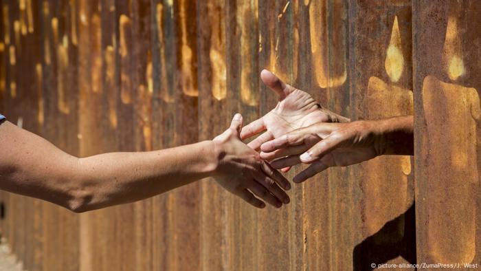 People stretch out their hands to each other between steel barriers on the border between the United States and Mexico.