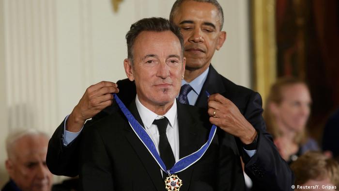 Barack Obama steht hinter Bruce Springsteen und legt ihm eine Medaille um.