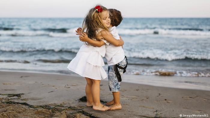 Two kids hugging on a beach (Imago/Westend61)