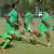 Team members of the Zimbabwe Warriors wearing green uniforms with yellow stripes run across a field.