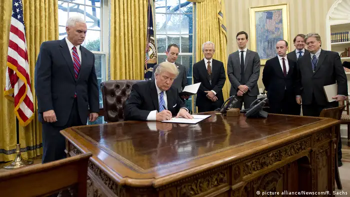 Trump signs executive order on his desk in the Oval office while advisers look on (picture alliance/Newscom/R. Sachs)