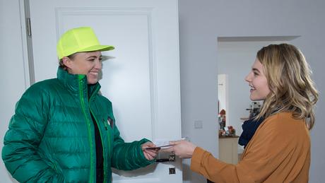 A delivery woman brings the pizzas that Sebastian has ordered to the apartment.