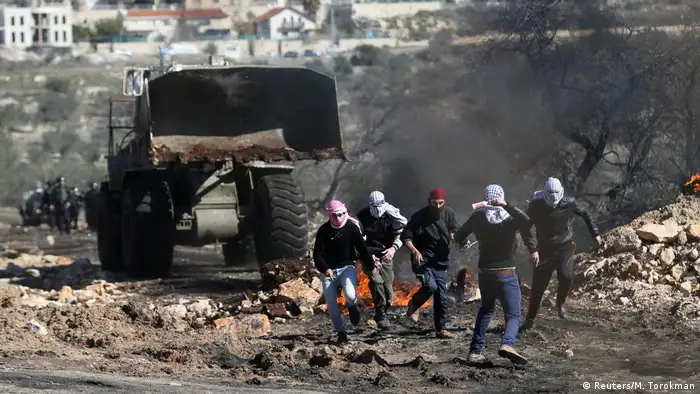 Vermummte Jugendlichen rennen vor Polizisten weg. Schutt liegt auf der Straße und ein großes Feuer brennt hinter einem LKW. (Foto: Reuters/M. Torokman)