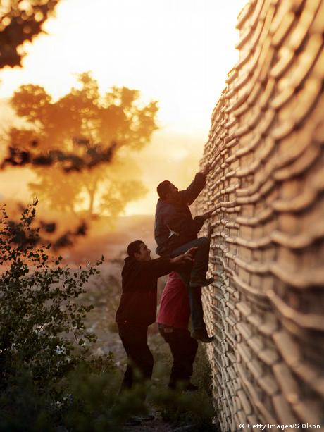 Símbolo del aislamiento. Migrantes latinoamericanos escalan la valla fronteriza.