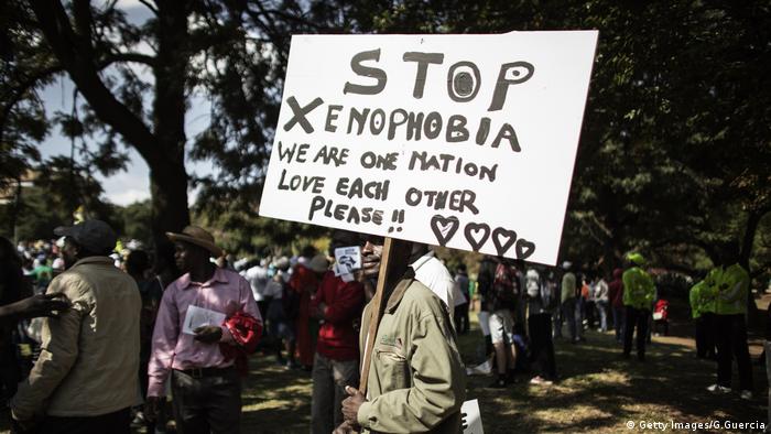 A South African demonstrator holds a banner reading Stop Xenophobia. We are one nation. Love each other please!!