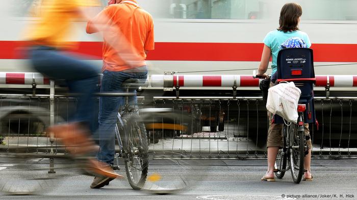 Some cyclists wait for a train to pass by. 