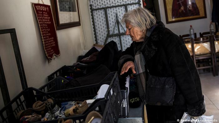 An elderly woman searches through donated clothes at a soup kitchen.
