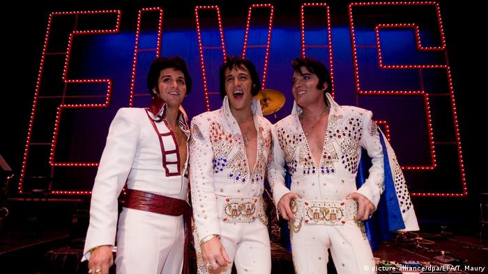 Elvis doubles wearing white suits with Elvis sign in background