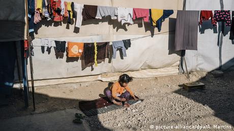 Child sitting on stony ground, laundry fluttering on lines overhead (picture-alliance/dpa/A. Martins)