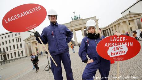 A male and a femal construction worker showing the difference in their pay during a protest in front of Berlin's landmark Brandenburg Gate