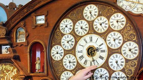شخص يضبط الساعة الكبيرة بأصابعه، التي تحيطها ساعات أصغر تشير إلى من مناطق زمنية أخرى في العالم.
