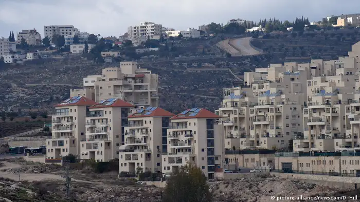 Apartment houses stand in desert land in an Israeli settlement while Palestinian houses stand atop a hill in the background (picture-alliance/newscom/D. Hill)