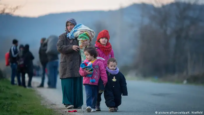 Refugees in Greece walk along a road, bundled up against the cold