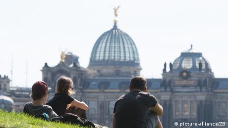 Drei junge Menschen sitzen in Dresden auf den Elbwiesen vor der Hochschule für Bildende Künste.