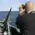 Član posade vojnog broda stoji na brodu i promatra okolinu kroz dalekozor