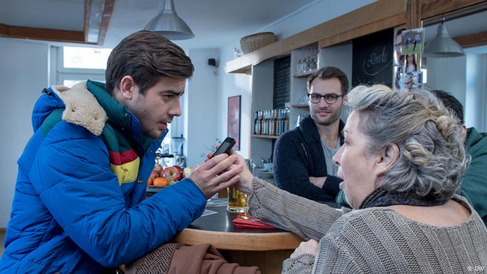 Eine ältere Frau zeigt einem jungen Mann ihr Smartphone.