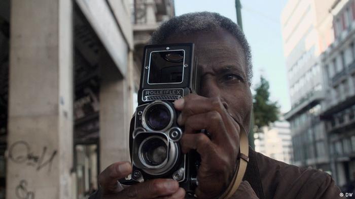 Akinbode Akinbiyi, man holds a small camera up to his face 
