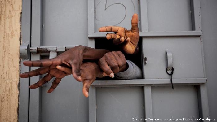 Manos de refugiados pididendo ayuda a través de una puerta en Libia.