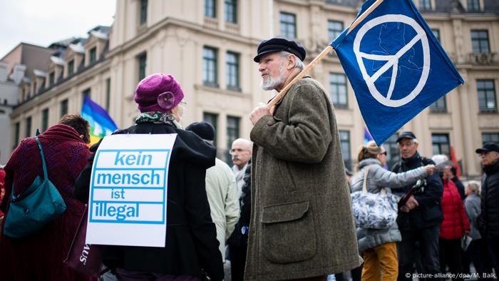 Frau mit Kein Mensch ist illegal-Schriftzug auf dem Rücken, daneben ein Mann mit Peacefahne beim Ostermarsch in München. (picture-alliance/dpa/M. Balk)