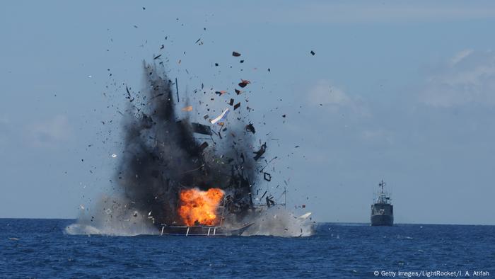 Sebuah kapal meledak di laut lepas setelah dibom oleh kapal angkatan laut Indonesia (di latar belakang)