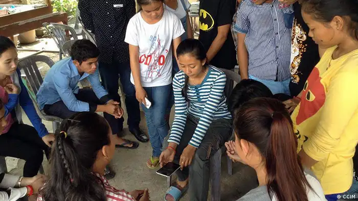 Several young people are grouped around a young Cambodia woman holding a smart phone