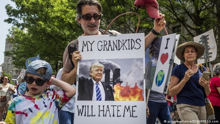 A climate protester holds a sign showing Donald Trump in front of a coal factory 