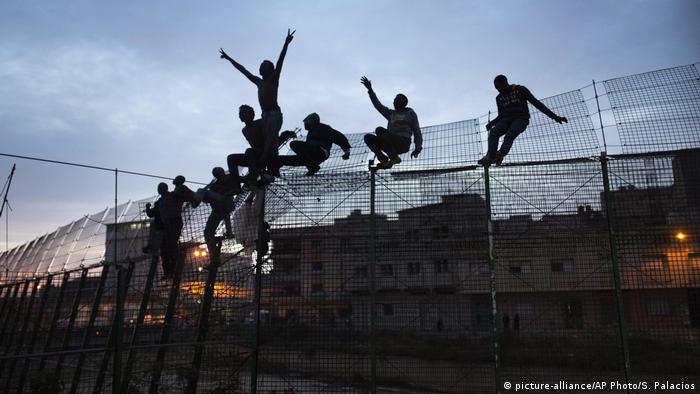 A group of people from sub-Saharan countries climb over a fence between Morocco and Spain's North African enclave of Melilla