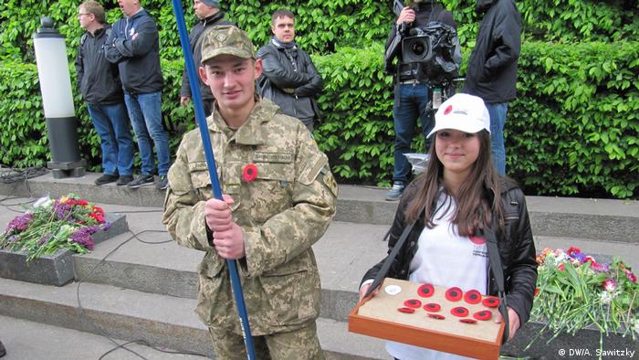 Парень в камуфляже с красным маком на груди и девушка, раздающая красные маки