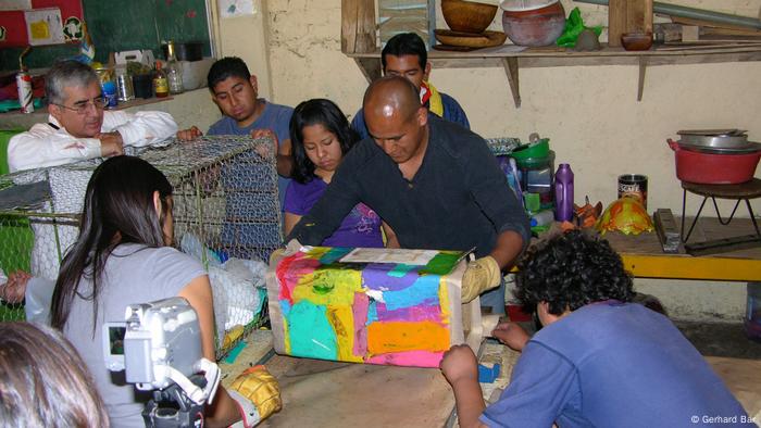 Un grupo de jóvenes mexicanos observa como una persona moldea un bote de polietileno reciclado.