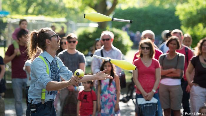 Ein Jongleur beim Straßenfest des Karnevals der Kulturen in Berlin 2016. Im Hintergrund sind Zuschauer zu sehen: Männer, Frauen, Kinder. (Foto: Frank Löhmer)