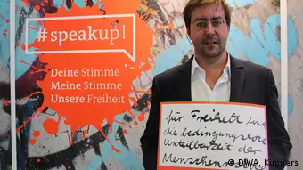 Christian Mihr hält ein Schild mit der Aufschrift für Freiheit und die bedingungslose Unteilbarkeit der Menschenrechte in die Kamera.
