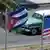 Carro antigo passa em uma rua. Em primeiro plano, uma bandeira dos EUA e uma bandeira de Cuba tremulando. 