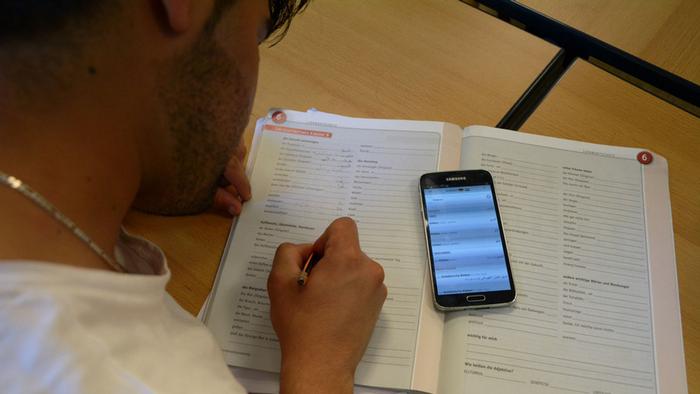 A student looks at workbook and his smartphone to do his homework