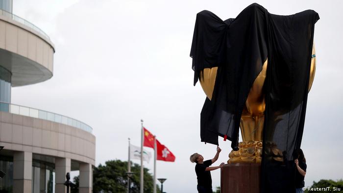 Pro-democracy activists cover the Golden Bauhinia with black cloth to demand full democracy ahead of 20th anniversary of the handover from British to China