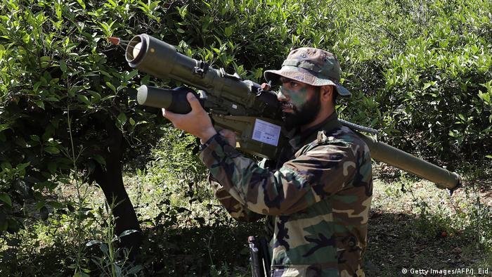 A Hezbollah fighter stands with a rocket launcher in a grove of trees