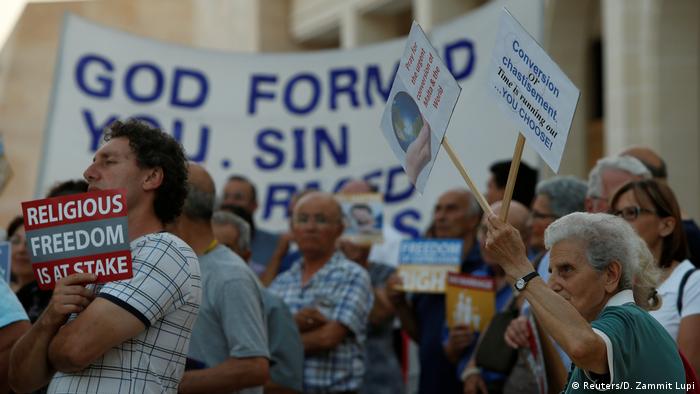 Protesters wave signs outside the parliament in Valletta the day before the final vote on gay marriage