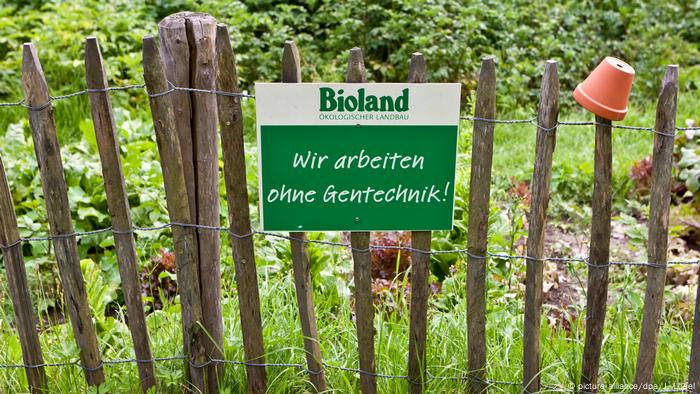 Uma placa da Bioland está pendurada em uma cerca de madeira em frente a uma horta