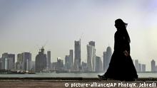 FILE- In this May 14, 2010 file photo, a Qatari woman walks in front of the city skyline in Doha, Qatar. Qatar likely faces a deadline this weekend to comply with a list of demands issued to it by Arab nations that have cut diplomatic ties to the energy-rich country, though its leaders already have dismissed the ultimatum. (AP Photo/Kamran Jebreili, File) |