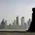 A veiled woman walks in front of the city skyline in Doha