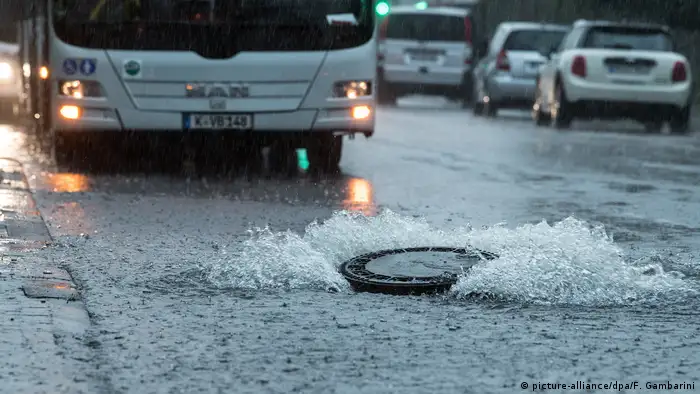 Der Deckel eines Gullys wird auf einer überfluteten Straße in Köln (Nordrhein-Westfalen) vom Wasserdruck hochgehoben. (Foto: picture-alliance/dpa/F. Gambarini)