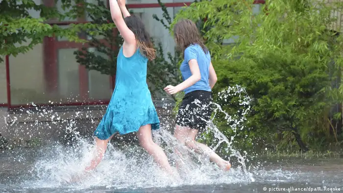 Zwei junge Frauen springen am 22.07.2017 durch vom Regen überschwemmte Wege in Hennigsdorf (Brandenburg). (Foto: picture-alliance/dpa/R. Roeske)