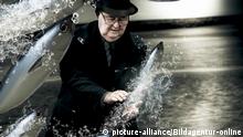 Artistic And Creative Photo Of A School Of Fish Splashing By A Senior Man Trying His Hand A Fishing For A Catch In A Plenty Of Fish In The Sea Conceptual | Verwendung weltweit, Keine Weitergabe an Wiederverkäufer.